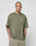 A person with a shaved head and tattoos wears the olive green LIVE FAST DIE YOUNG Basic +49 Chest Tee, made from 100% Baumwolle, and light shorts, standing against a white background with hands in pockets.