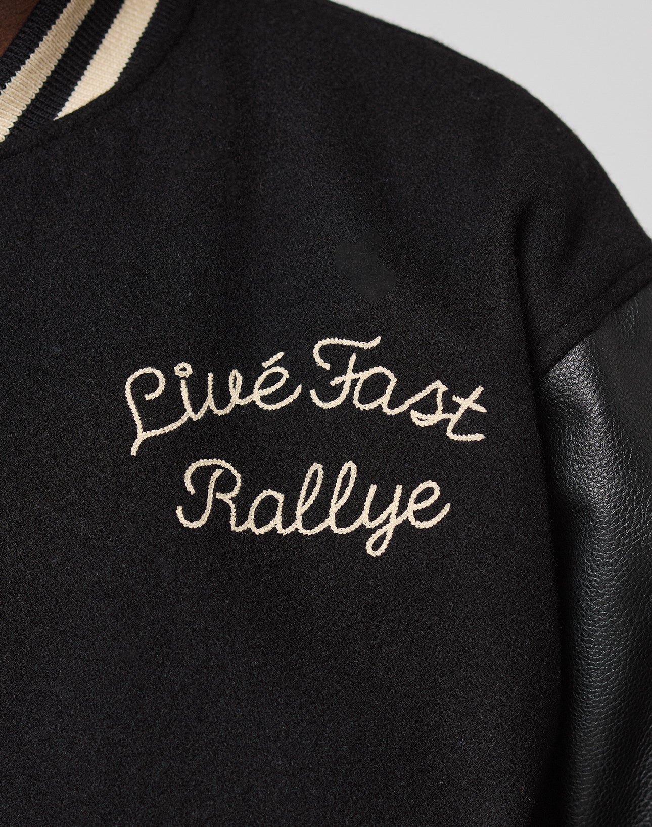 Close-up of the LFDY x Schott NYC Varsity Jacket by LIVE FAST DIE YOUNG, featuring cream Livé Fast Rallye embroidery on the chest, a black leather sleeve, and a striped collar.
