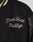 Close-up of the LFDY x Schott NYC Varsity Jacket by LIVE FAST DIE YOUNG, featuring cream Livé Fast Rallye embroidery on the chest, a black leather sleeve, and a striped collar.