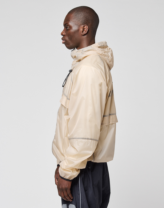 A man in profile wears the LIVE FAST DIE YOUNG Live Fast Nylon Jacket in light beige with reflective print and dark pants, set against a plain light gray background.