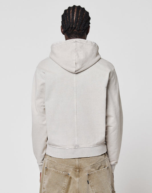 A person with braided hair faces away from the camera, wearing a light beige LFDY Corp. Hooded Zip by LIVE FAST DIE YOUNG and tan pants, standing against a plain white background.