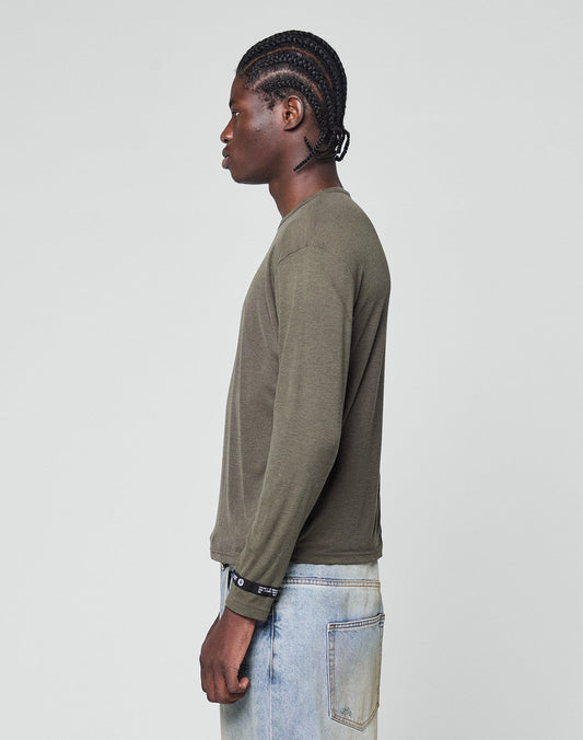 A person with braided hair stands in profile against a plain background, wearing the LIVE FAST DIE YOUNG LFDY Rib Longsleeve in olive green and light blue jeans.