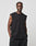 A man with cornrow braids wears the LIVE FAST DIE YOUNG Basic Muscle Shirt in black, made of 100% Baumwolle, paired with black pants. He stands against a white background with his hands in his pockets, looking confidently at the camera.