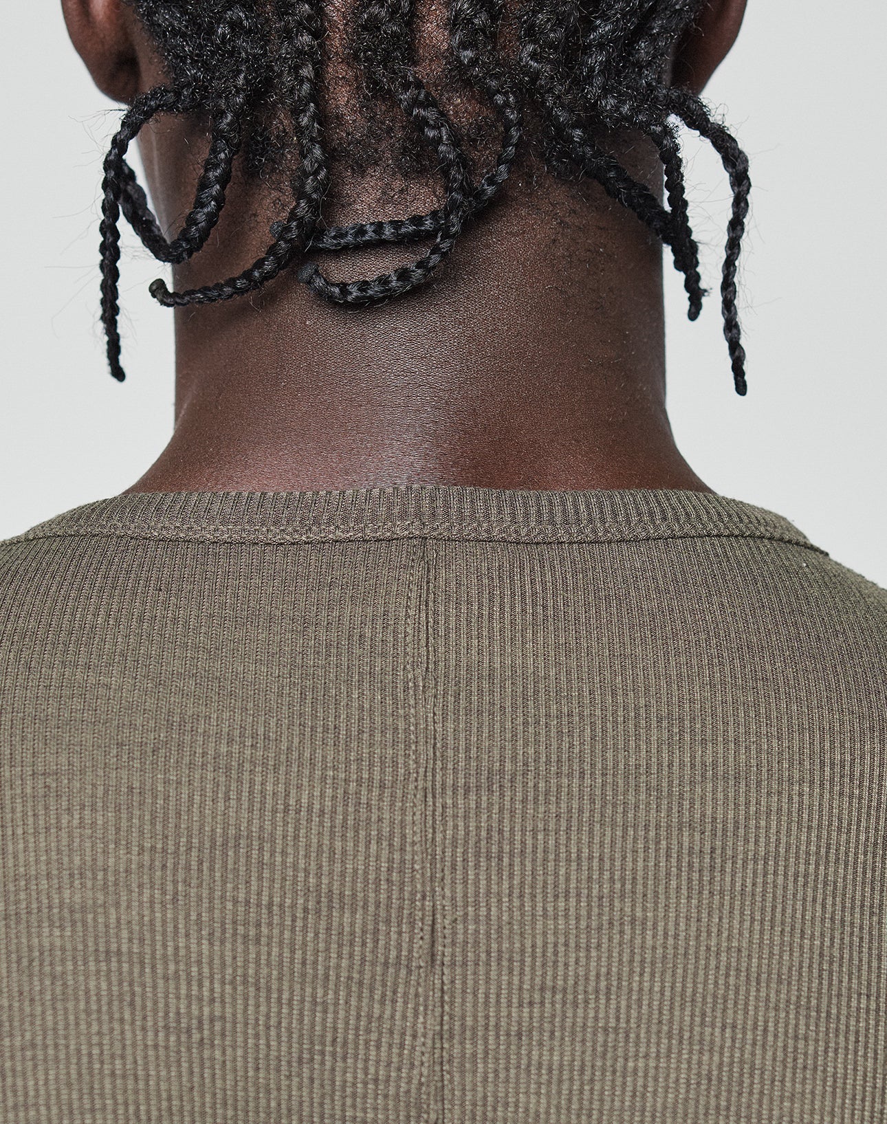 Close-up of a person's neck and shoulders with short twisted braids, wearing an oversized, ribbed olive-green LFDY Rib Longsleeve by LIVE FAST DIE YOUNG. Plain light background; a subtle web label adds modern detail.