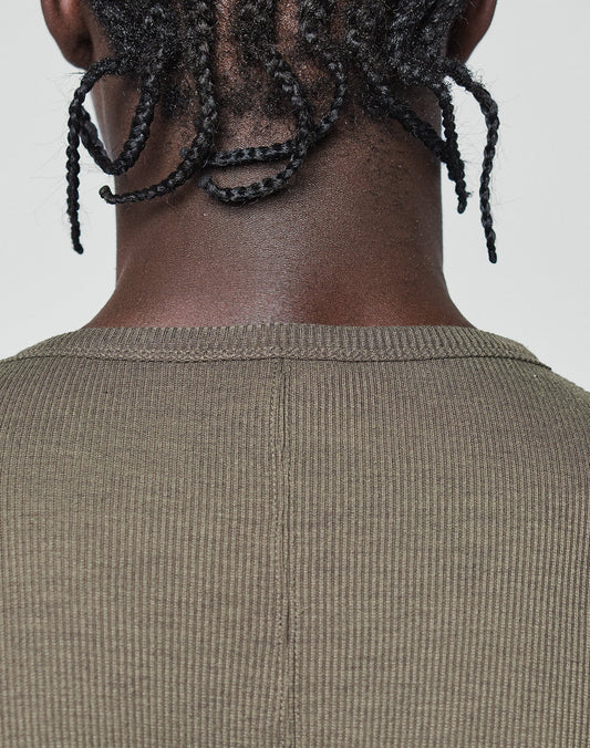 Close-up of a person's neck and shoulders with short twisted braids, wearing an oversized, ribbed olive-green LFDY Rib Longsleeve by LIVE FAST DIE YOUNG. Plain light background; a subtle web label adds modern detail.
