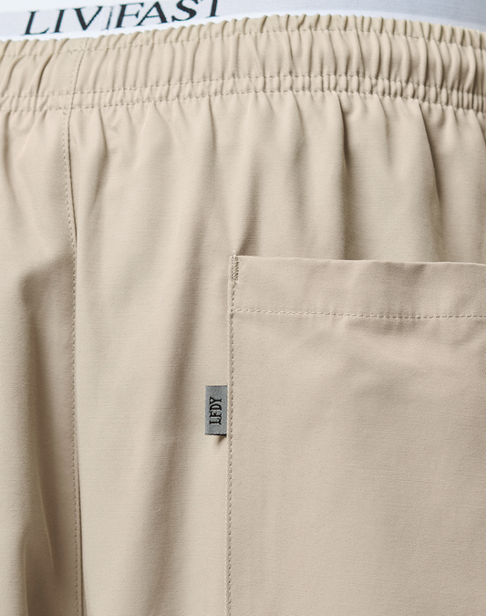Close-up of Baggy Nylon Pants by LIVE FAST DIE YOUNG featuring an elastic waistband, patch pockets, a visible side pocket, and a small fabric tag labeled TIBY. The LIVIFAST text is partially visible on the waistband.