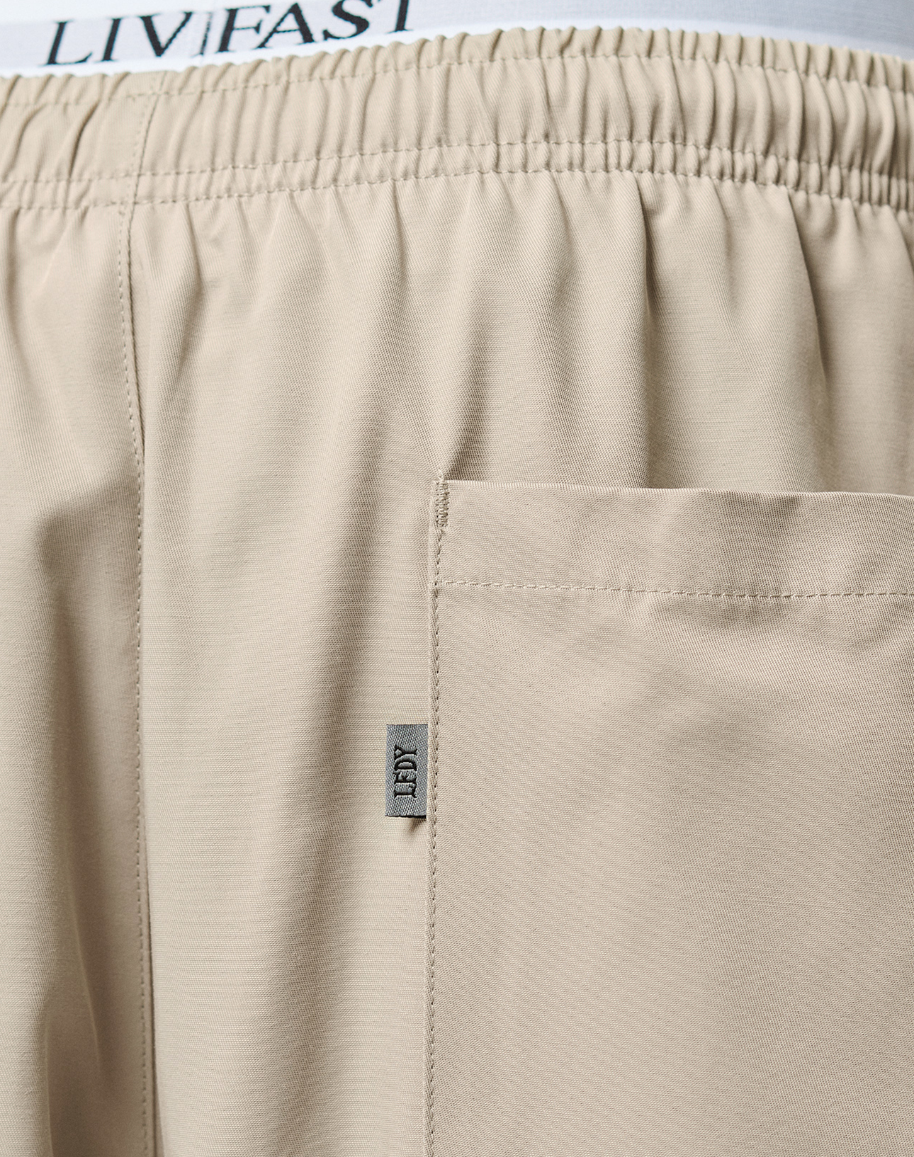 Close-up of Baggy Nylon Pants by LIVE FAST DIE YOUNG featuring an elastic waistband, patch pockets, a visible side pocket, and a small fabric tag labeled TIBY. The LIVIFAST text is partially visible on the waistband.