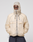 A person wearing the LIVE FAST DIE YOUNG Live Fast Nylon Jacket in light beige with reflective print, hood up and hands in pockets, stands against a plain light gray background.
