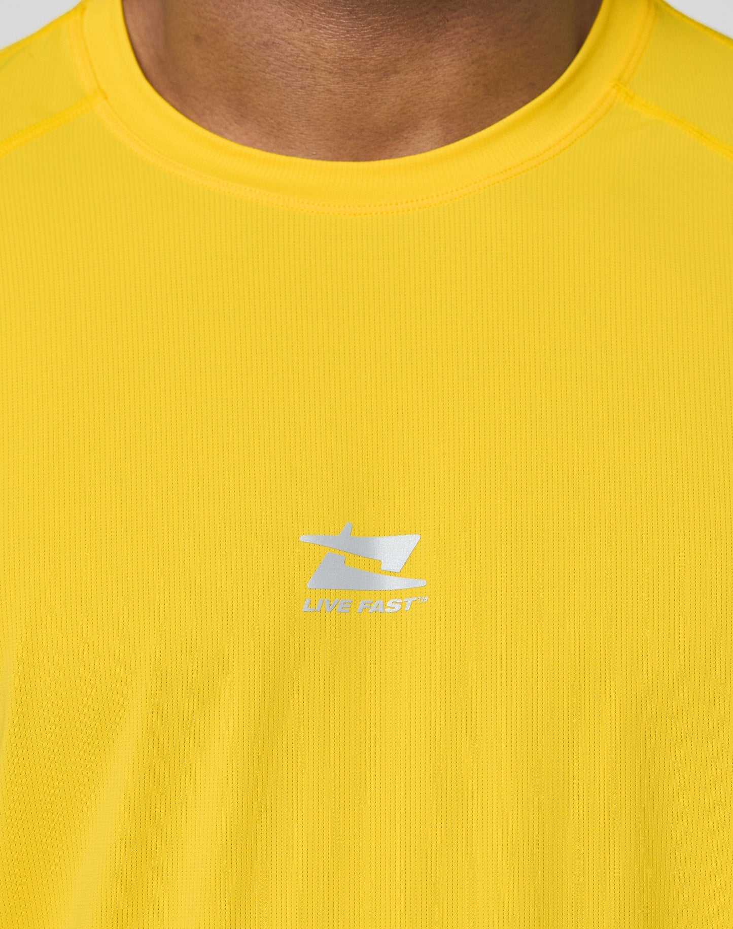 The Live Fast Performance Tee by LIVE FAST DIE YOUNG is a bright yellow, slim-fit short-sleeve athletic shirt made from a Nylon Spandex blend, with “LIVE” and “FAST” in small reflective print on the upper back.