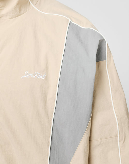 The Basic Nylon Trackjacket by LIVE FAST DIE YOUNG features a beige and light gray color block design, white piping, Live Fast embroidery on the left chest, regular fit, high collar, and is crafted from nylon and polyester.