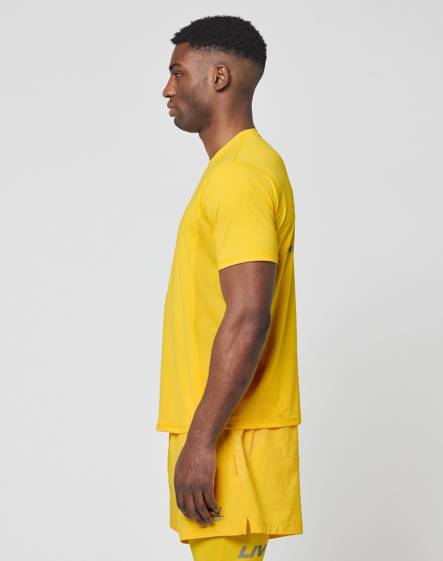 Close-up of a person in the LIVE FAST DIE YOUNG Live Fast Performance Tee, a bright yellow slim fit athletic shirt with a white LIVE FAST logo and reflective chest print. Only the lower face and upper chest are visible.