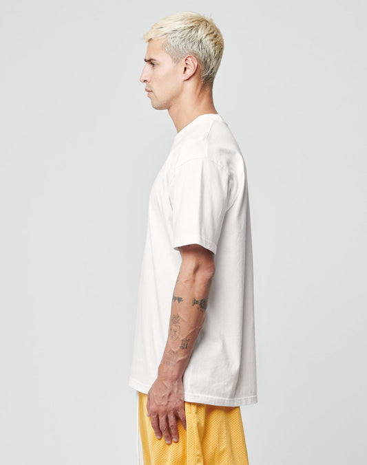 A person with short blond hair stands in profile, wearing a plain white LIVE FAST DIE YOUNG LFDY Fries Tee and yellow mesh shorts. Their tattooed arm is visible against a plain light gray background. Style: LF2406-15695.
