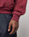 A close-up of a tattooed hand relaxed by the side, wearing the LIVE FAST DIE YOUNG Live Fast Stallion Hooded sweatshirt in maroon and dark blue jeans with white stitching.