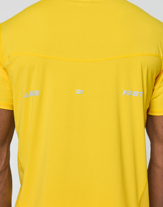 A person is shown from the upper back wearing the LIVE FAST DIE YOUNG Live Fast Performance Tee, a bright yellow slim fit shirt with LIVE and FAST printed in white and a small central logo.
