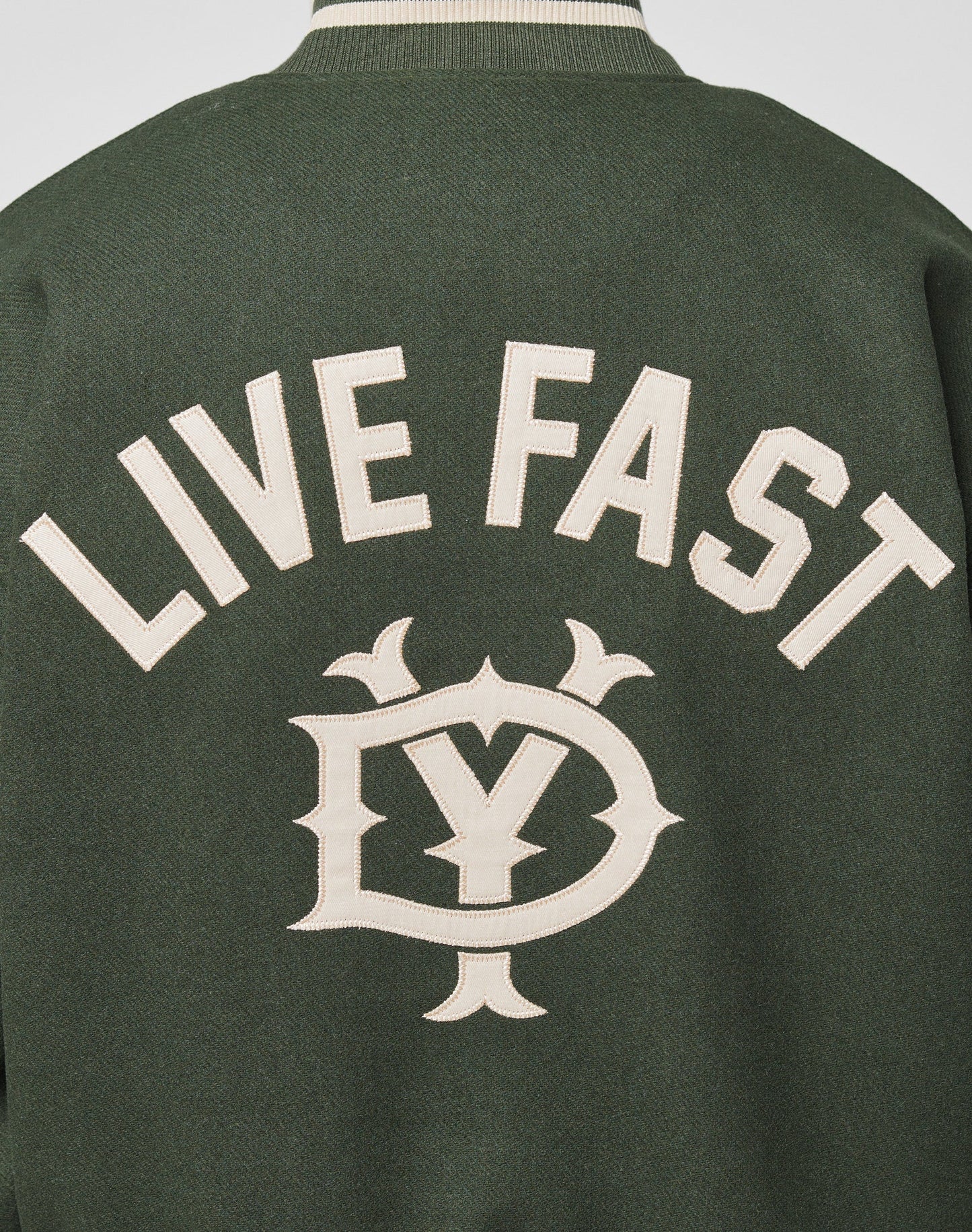 The Live Fast College Jacket by LIVE FAST DIE YOUNG has bold beige LIVE FAST lettering and a stylized emblem on the back, with striking contrast-color details for a standout dark green look.