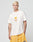 A man with short blond hair wears the LIVE FAST DIE YOUNG LFDY Fries Tee, a regular fit white t-shirt with a French fries graphic, and yellow basketball shorts. He stands against a light gray background, left hand in his pocket.