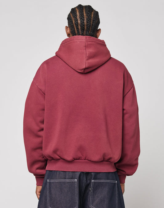 A person with braided hair is seen from behind, wearing the LIVE FAST DIE YOUNG Live Fast Stallion Hooded in maroon, featuring an oversize fit and soft polyester-cotton blend, paired with dark jeans against a plain light background.