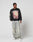 A man stands before a plain light background wearing the LFDY Angel Sweater by LIVE FAST DIE YOUNG, paired with oversized light-wash distressed cotton jeans and white sneakers. He looks left with one hand by his side, the other slightly raised.