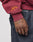 A person wearing the LIVE FAST DIE YOUNG Live Fast Stallion Hooded sweatshirt in maroon with yellow sleeve embroidery and dark jeans rests their tattooed, silver ring-adorned hand near their pocket.