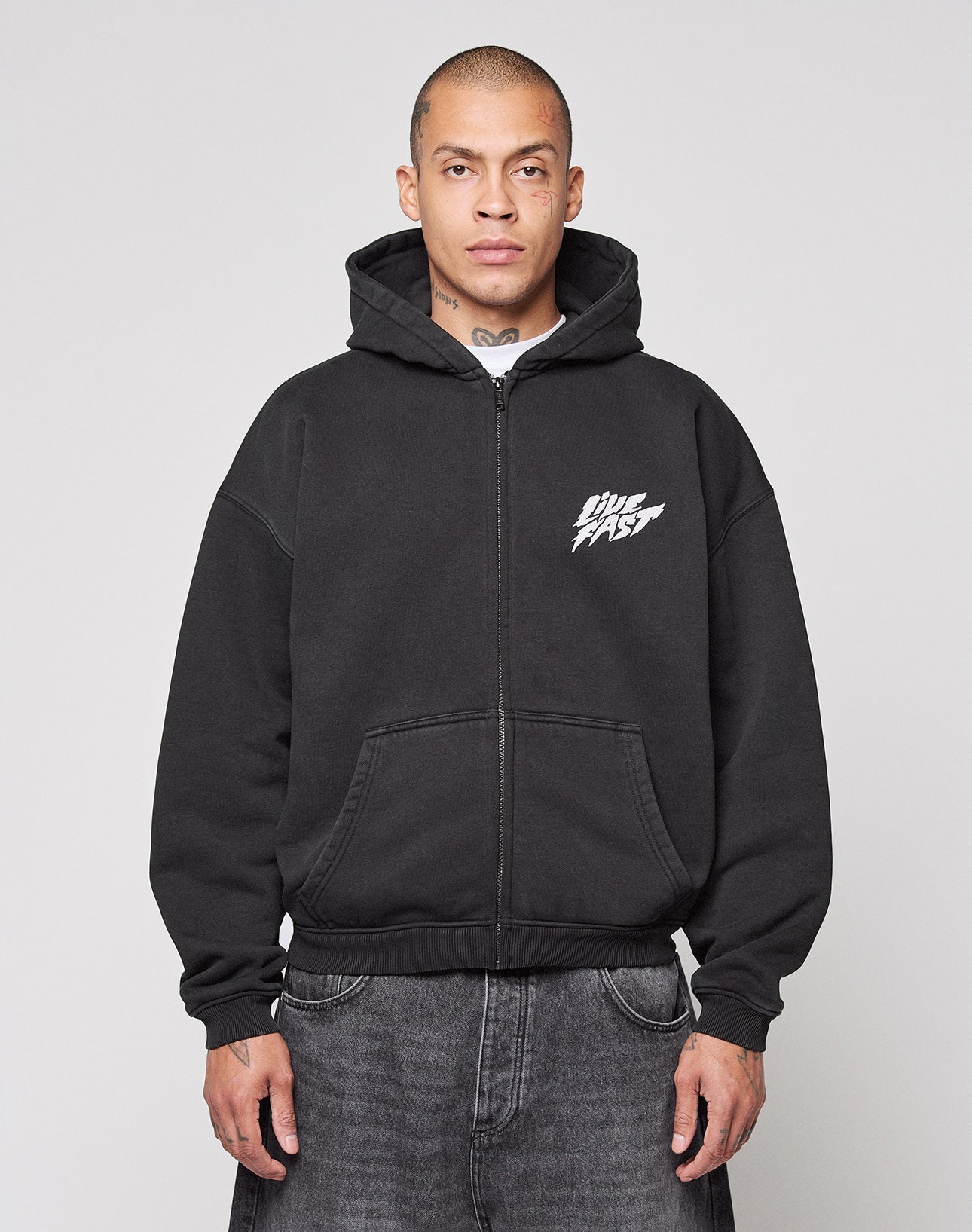 A person faces forward against a gray background, wearing the LIVE FAST DIE YOUNG LFDY Logo Hooded Zip in black with “ONE FAST” in white on the chest, featuring an Oversize Fit style.