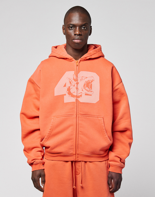 A person wearing the orange LFDY 40 Hooded Zip by LIVE FAST DIE YOUNG, featuring a large number 49 and shark front print, stands against a plain light gray background. | model