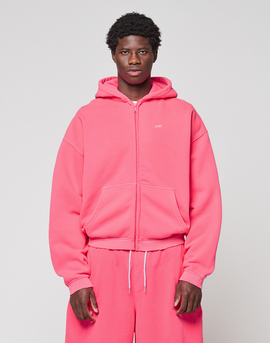 A person stands facing forward in an oversized bright pink LIVE FAST DIE YOUNG Basic Hooded Zip with matching sweatpants, set against a plain light gray background. | model