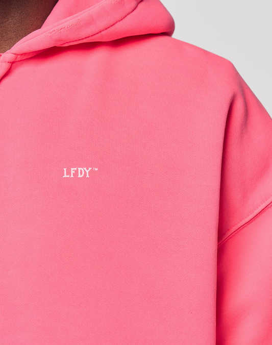 Close-up of a person wearing the LIVE FAST DIE YOUNG Basic Hooded Zip in bright pink with bold white branding on the chest. Only the shoulder, chest, and part of the hood are visible against a plain background.