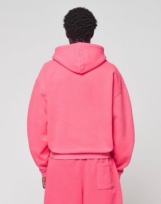A person faces away from the camera, wearing a bright pink LIVE FAST DIE YOUNG Basic Hooded Zip oversize hoodie and matching sweatpants with a pocket, set against a plain light background.