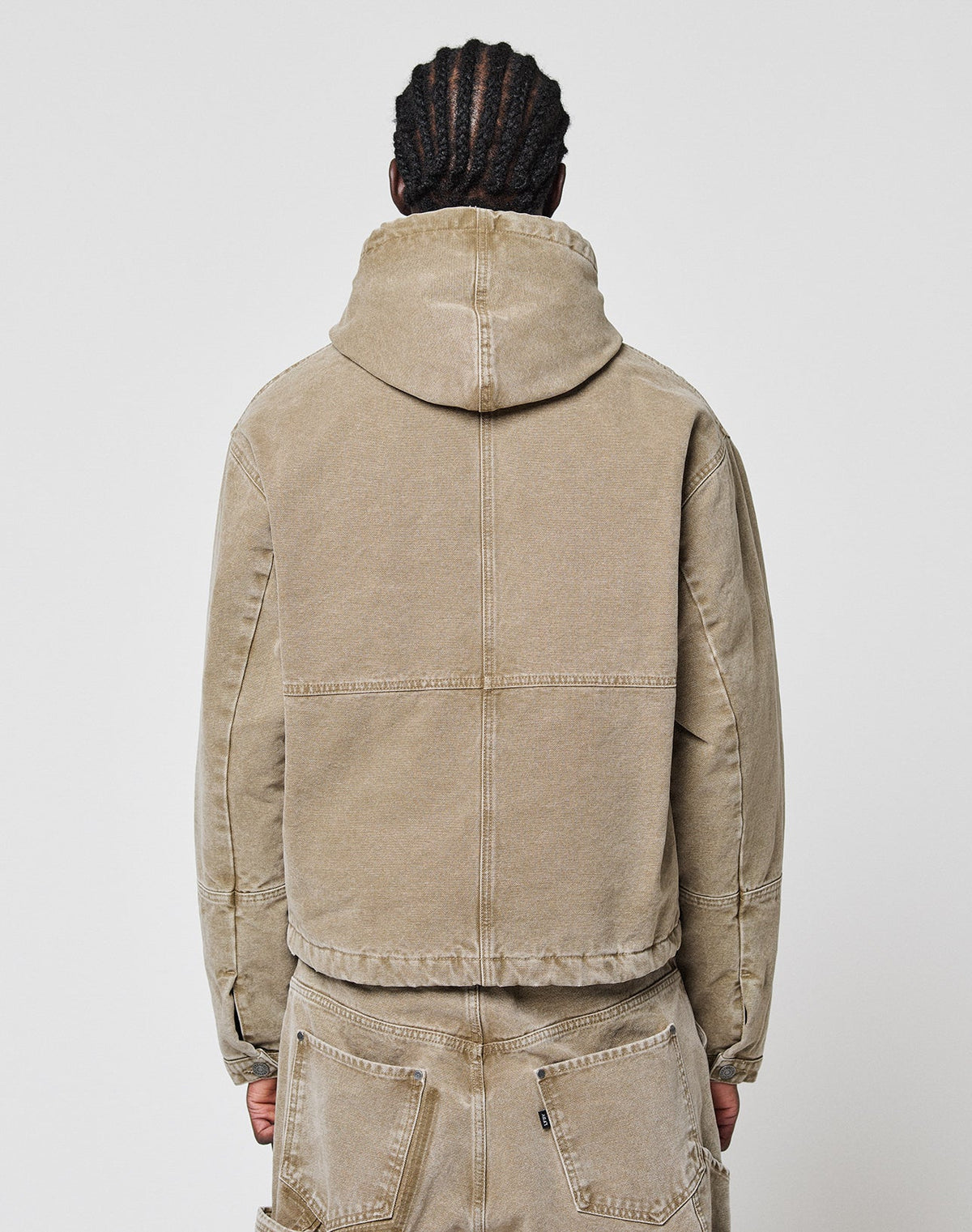 A person with braided hair is shown from the back, wearing a tan LIVE FAST DIE YOUNG Faded Workwear Jacket with matching pants against a plain white background.