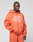 Someone wearing the LFDY 40 Hooded Zip by LIVE FAST DIE YOUNG, an oversized orange zip-up pullover with a frontprint graphic number 42 and animal head, paired with matching orange sweatpants, stands against a plain light gray background.