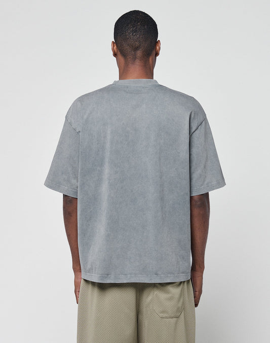 A man with short hair, facing away from the camera, wears the LIVE FAST DIE YOUNG Basic +49 Chest Tee in an oversize faded gray style and light beige shorts against a plain white background.