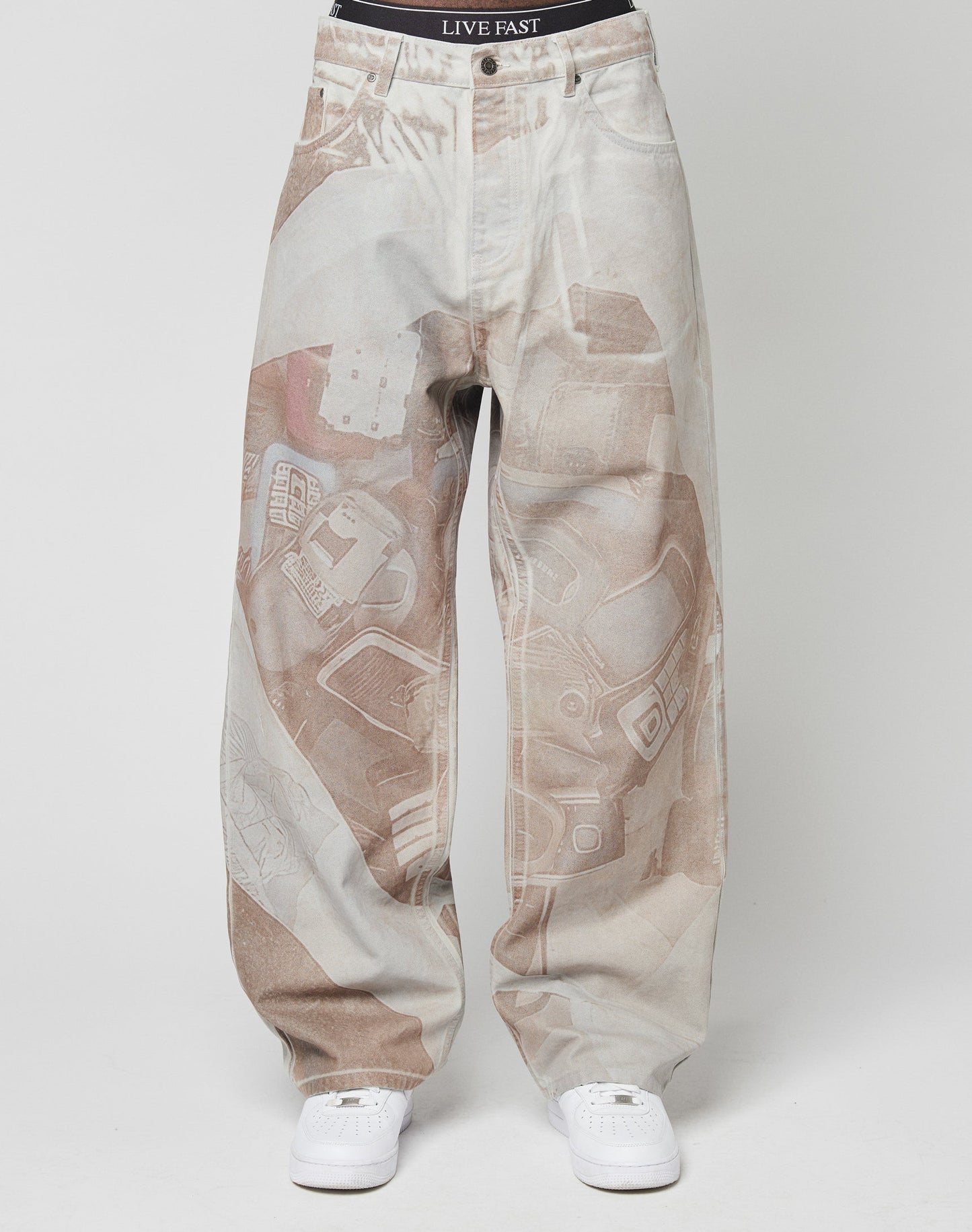 A person wears baggy, light-colored LFDY Stolen Phones Denim by LIVE FAST DIE YOUNG with an abstract all-over print and white sneakers. The waistband of black LIVE FAST DIE YOUNG underwear is visible above the pants.