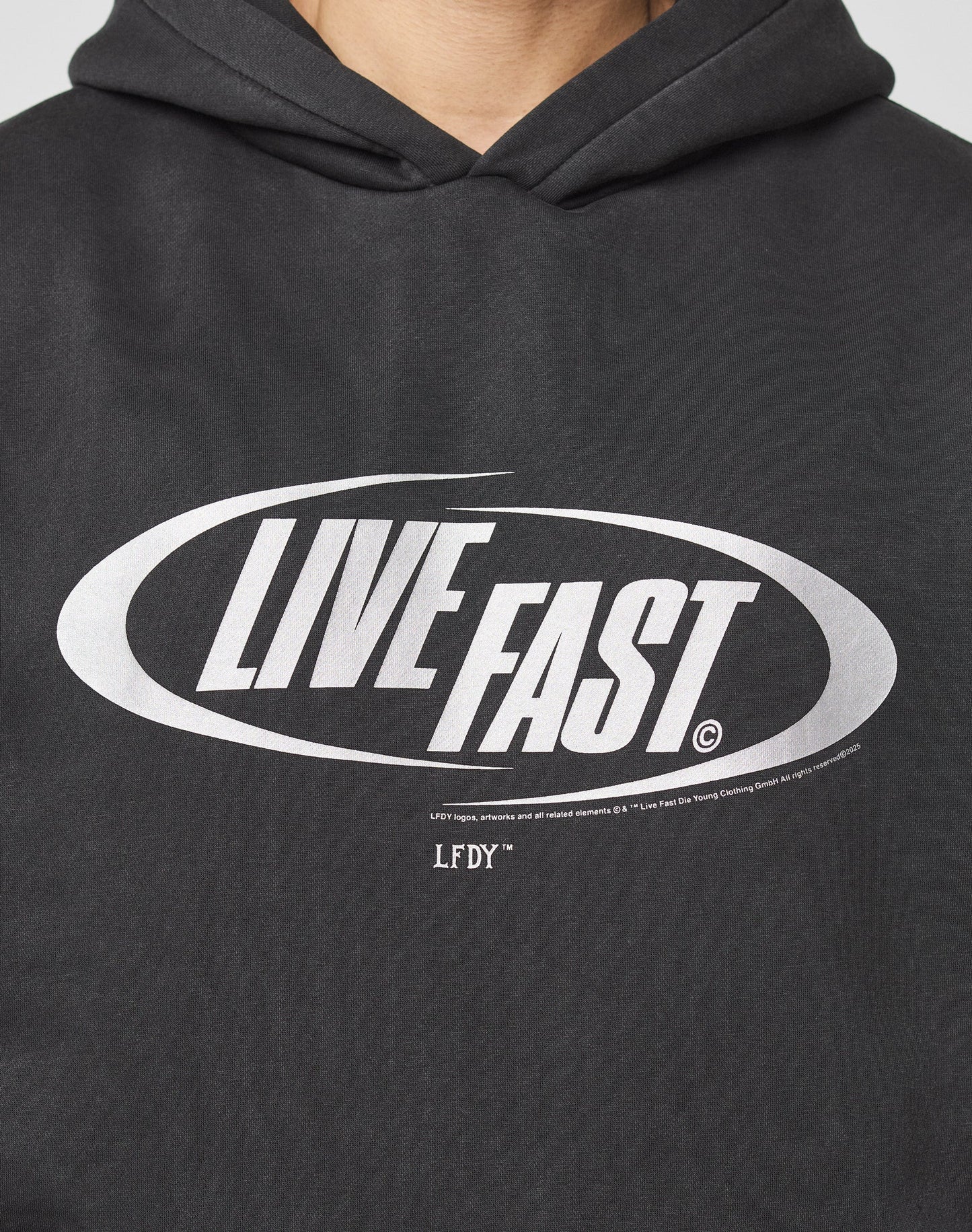 Someone wears the LFDY Sphere Hooded by LIVE FAST DIE YOUNG, an oversize black cotton hoodie with LIVE FAST in bold silver oval front print and LFDY below in smaller text.