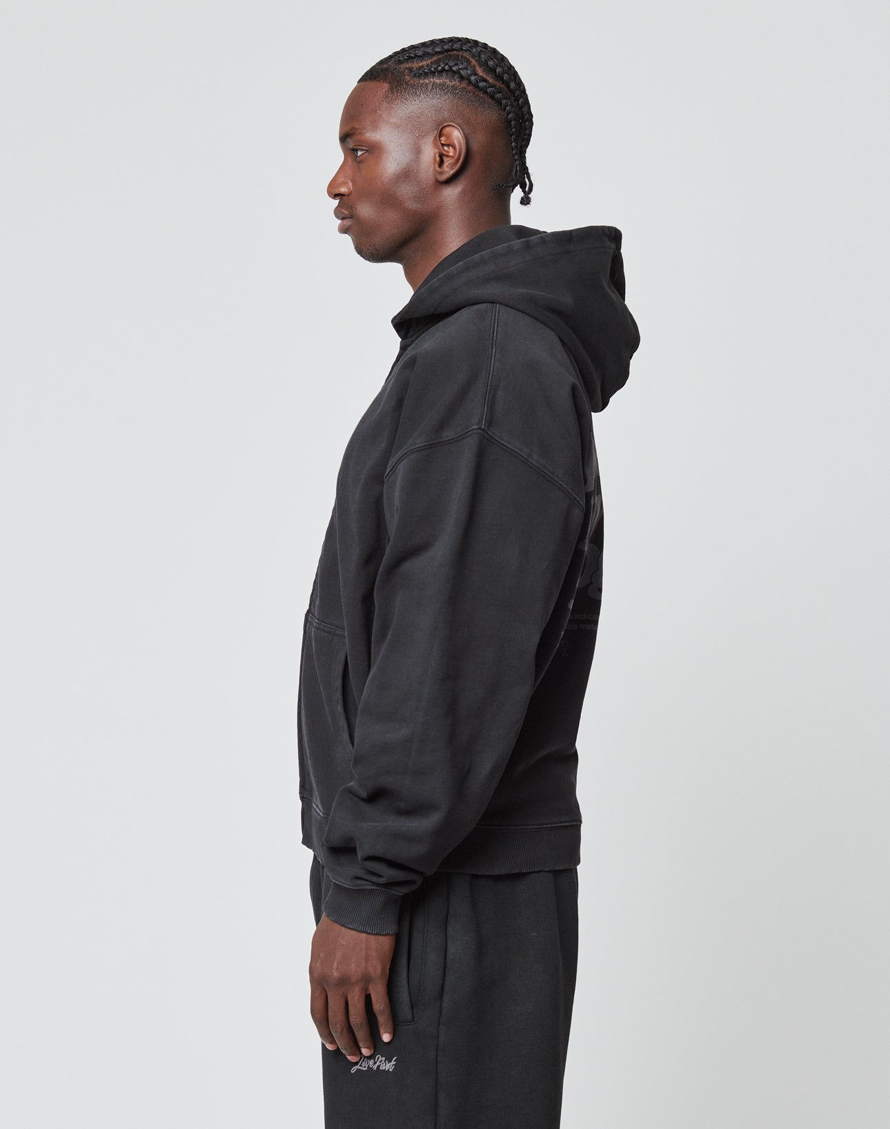 A person stands in profile, facing left, wearing the LIVE FAST DIE YOUNG Basic 510 Hooded Zip in Oversize Fit with matching black pants against a plain light gray background.