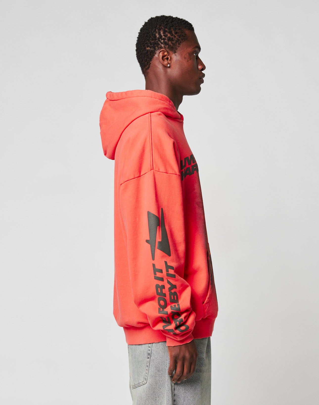 A person stands in profile against a plain light background, wearing the LIVE FAST DIE YOUNG LFDY Angel Hooded sweatshirt in bright red with black graphics on the sleeve and chest, paired with light gray jeans.