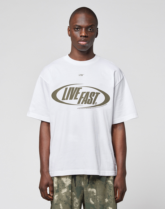 A person wears the LFDY Sphere Tee by LIVE FAST DIE YOUNG, a white oversize cotton T-shirt with "LIVE FAST" in bold inside an oval, featuring front and back prints, paired with camouflage pants.
