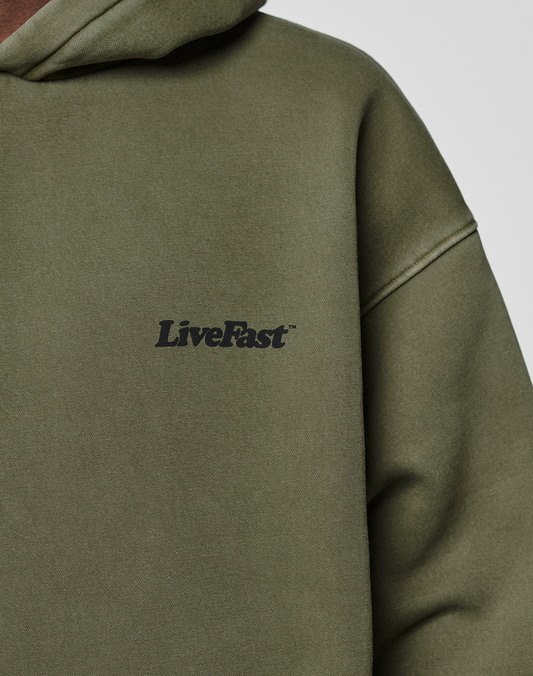 Close-up of the Basic 360 Hooded by LIVE FAST DIE YOUNG in olive green, featuring soft fabric, subtle topstitching, and black LiveFast™ text on the chest. The hood is partially visible at the upper left.