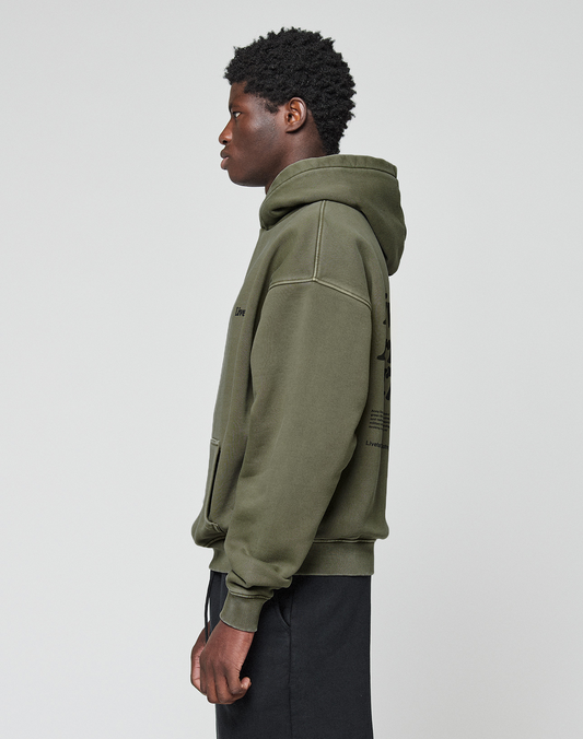 A young man with short curly hair stands in profile against a light gray background, wearing the LIVE FAST DIE YOUNG Basic 360 Hooded in olive green and black pants.