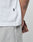 A close-up of a person in the LIVE FAST DIE YOUNG Basic +49 Tee in white, made from weicher Baumwolle, and light gray shorts. The shirt has a black tag; a forearm tattoo is visible as their hand rests at their side.