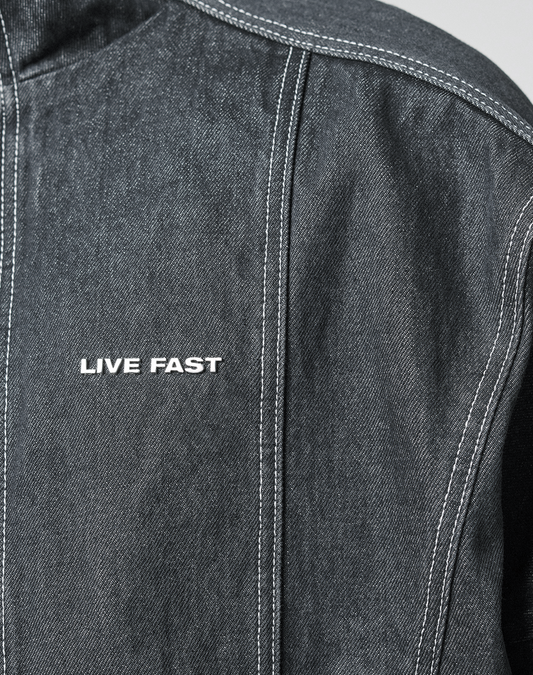 Close-up of the LFDY Denim Trackjacket by LIVE FAST DIE YOUNG: dark denim with Stehkragen, white stitching, and "LIVE FAST" embroidered on the front. Made from 100% Baumwolle with detailed craftsmanship.