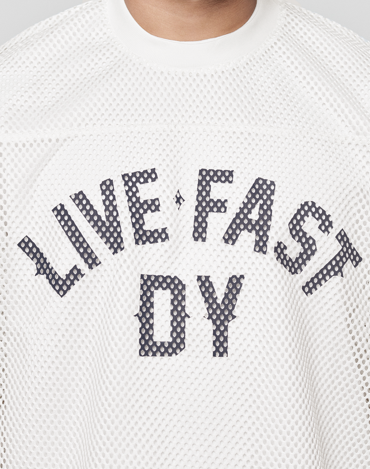 A close-up of the LFDY Boxy Jersey from LIVE FAST DIE YOUNG shows the white mesh fabric and bold "LIVE FAST DY" front print. The model’s neck and lower face are visible, emphasizing the tee’s boxy fit.