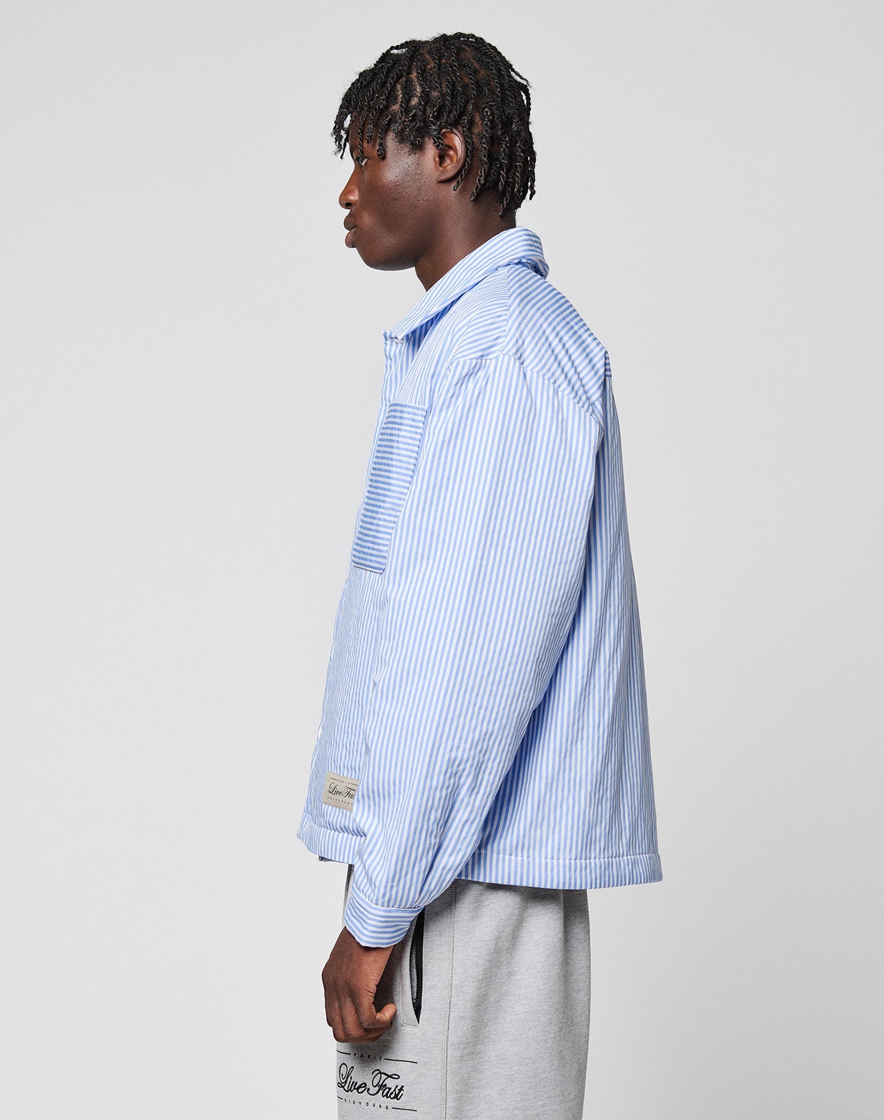 A person in profile against a plain background wears the LIVE FAST DIE YOUNG LFDY Striped Padded Shirt, styled as a button-up, paired with light gray sweatpants featuring black text near the pocket.