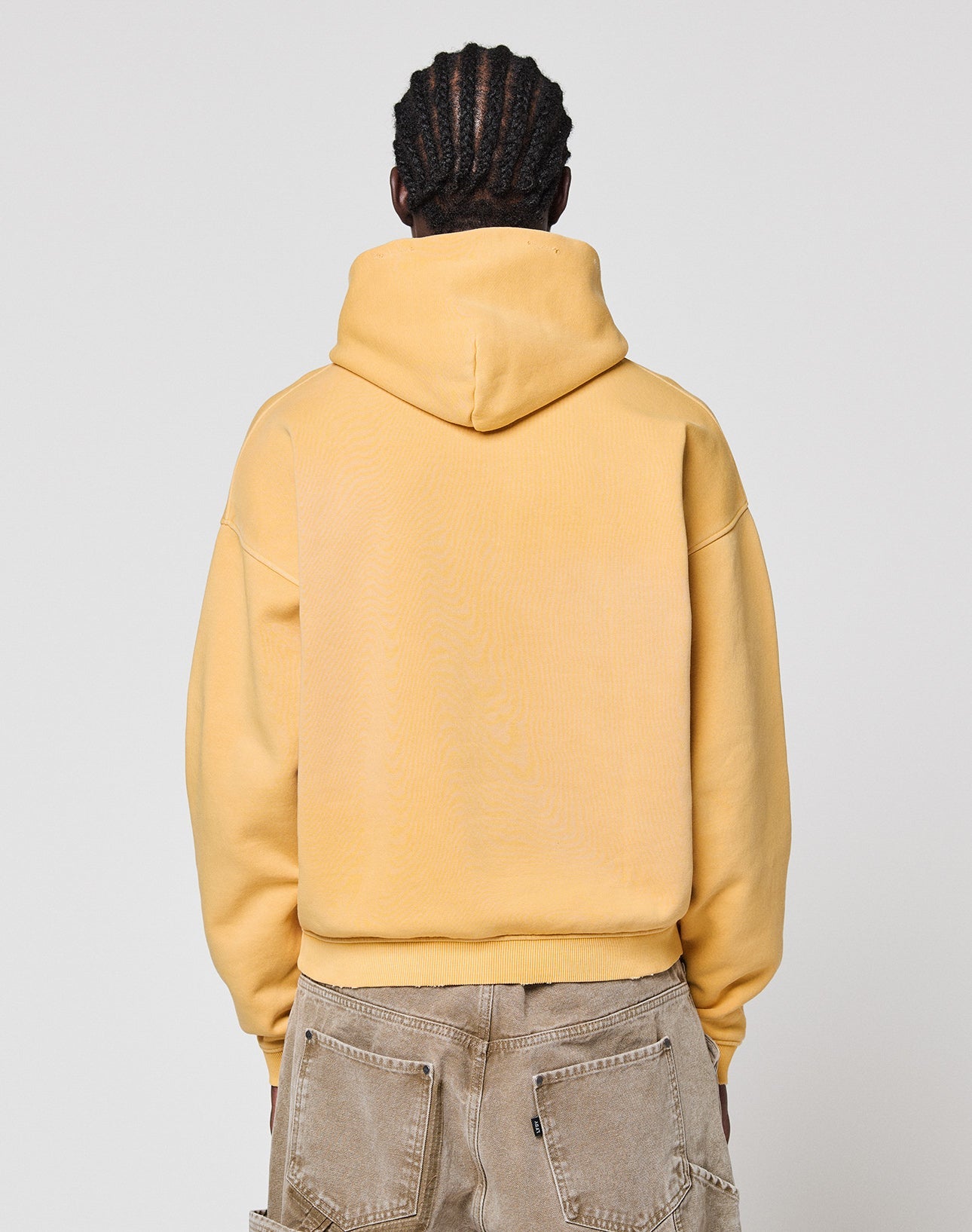 A person with braided hair is shown from the back wearing a yellow LFDY Corp. Hooded sweatshirt by LIVE FAST DIE YOUNG and light brown pants against a plain light gray background.
