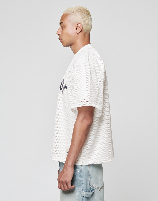 A person with short bleached blond hair stands in profile, wearing the LIVE FAST DIE YOUNG LFDY Boxy Jersey and light blue distressed jeans against a plain light background.