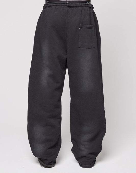 A person models the LIVE FAST DIE YOUNG Live Fast Rhinestone Jogger, featuring a wide fit, high waist, black color, and single front pocket. Their upper body is not visible as they stand against a plain white background.