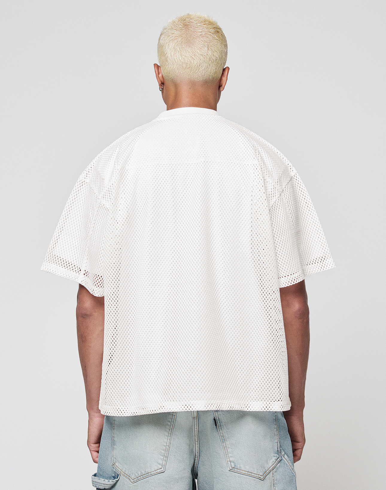A person with short, bleached blond hair is seen from behind wearing a LIVE FAST DIE YOUNG LFDY Boxy Jersey and light blue denim shorts against a plain gray background.