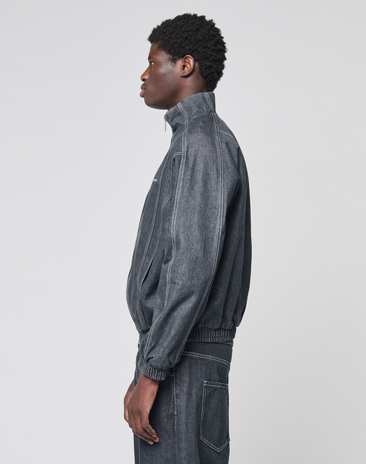A person in profile wears the LIVE FAST DIE YOUNG LFDY Denim Trackjacket, a dark gray 100% Baumwolle jacket with Stehkragen, zip-up front, white stitching, elastic waistband and cuffs, paired with matching pants.