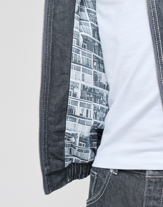A person wears the LFDY Denim Trackjacket by LIVE FAST DIE YOUNG, featuring a Stehkragen, black-and-white cityscape lining, and 100% Baumwolle. Paired with a white shirt and denim jeans; only the torso and part of one arm are visible.