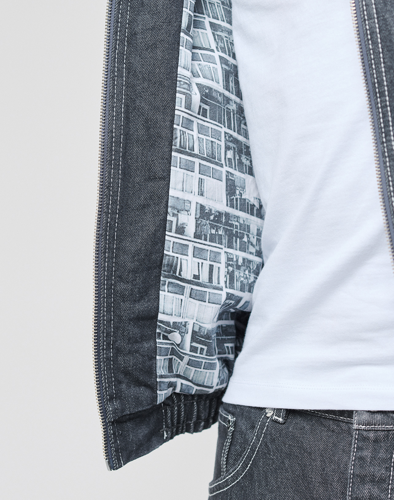 A person wears the LFDY Denim Trackjacket by LIVE FAST DIE YOUNG, featuring a Stehkragen, black-and-white cityscape lining, and 100% Baumwolle. Paired with a white shirt and denim jeans; only the torso and part of one arm are visible.