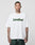 A person with short hair and visible tattoos wears the LIVE FAST DIE YOUNG Basic Tee, an oversize white T-shirt made from 100% Baumwolle with a bold green LiveFast frontprint, paired with dark green pants, against a plain background.